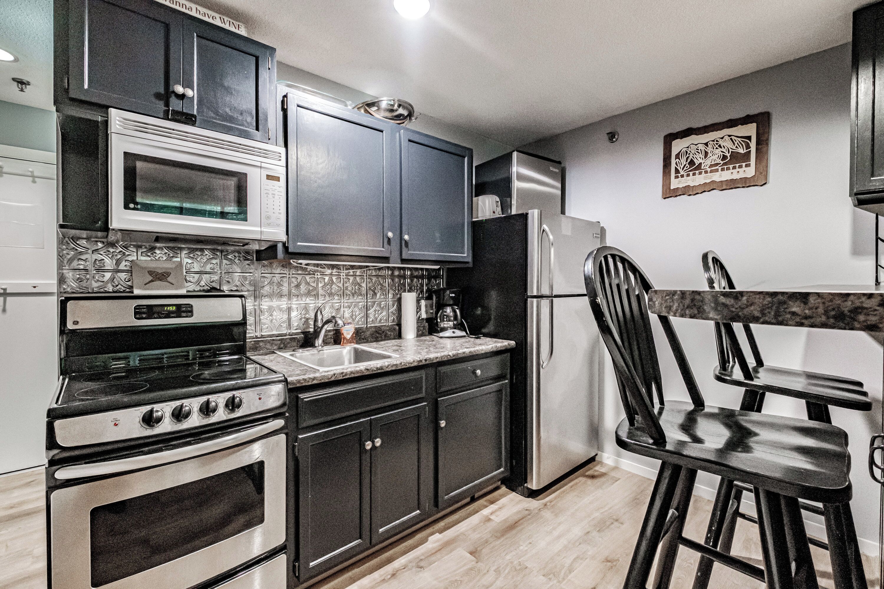 A kitchen with dark cabinets, a stainless steel refrigerator, a microwave, and a stove.