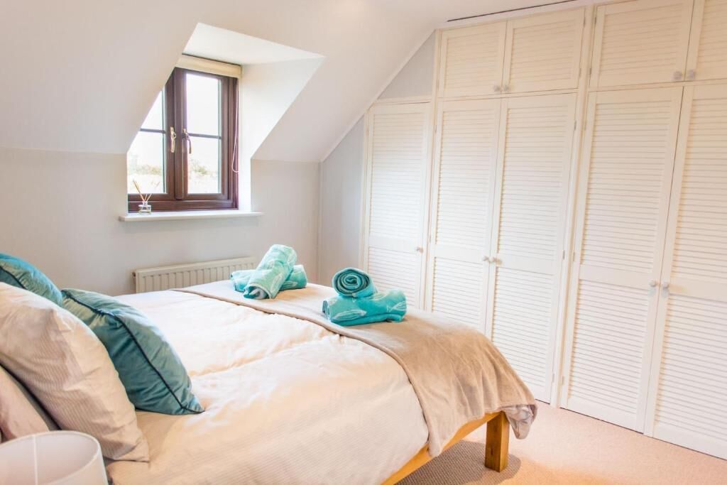 Een slaapkamer met een bed, een raam en een aantal witte kasten.
