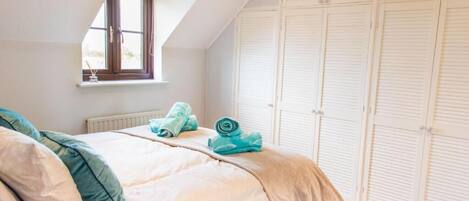 Een slaapkamer met een bed, een raam en een aantal witte kasten.