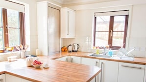 A modern kitchen with white cabinets, a wooden countertop, and a window providing natural light. - Host & Stay | Laylands Yard (Wells-next-the-Sea)