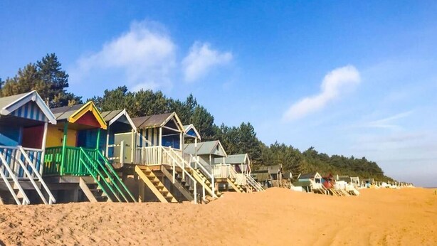 A row of beach huts with steps leading up to them, set against a clear blue sky. - Host & Stay | Laylands Yard (Wells-next-the-Sea)