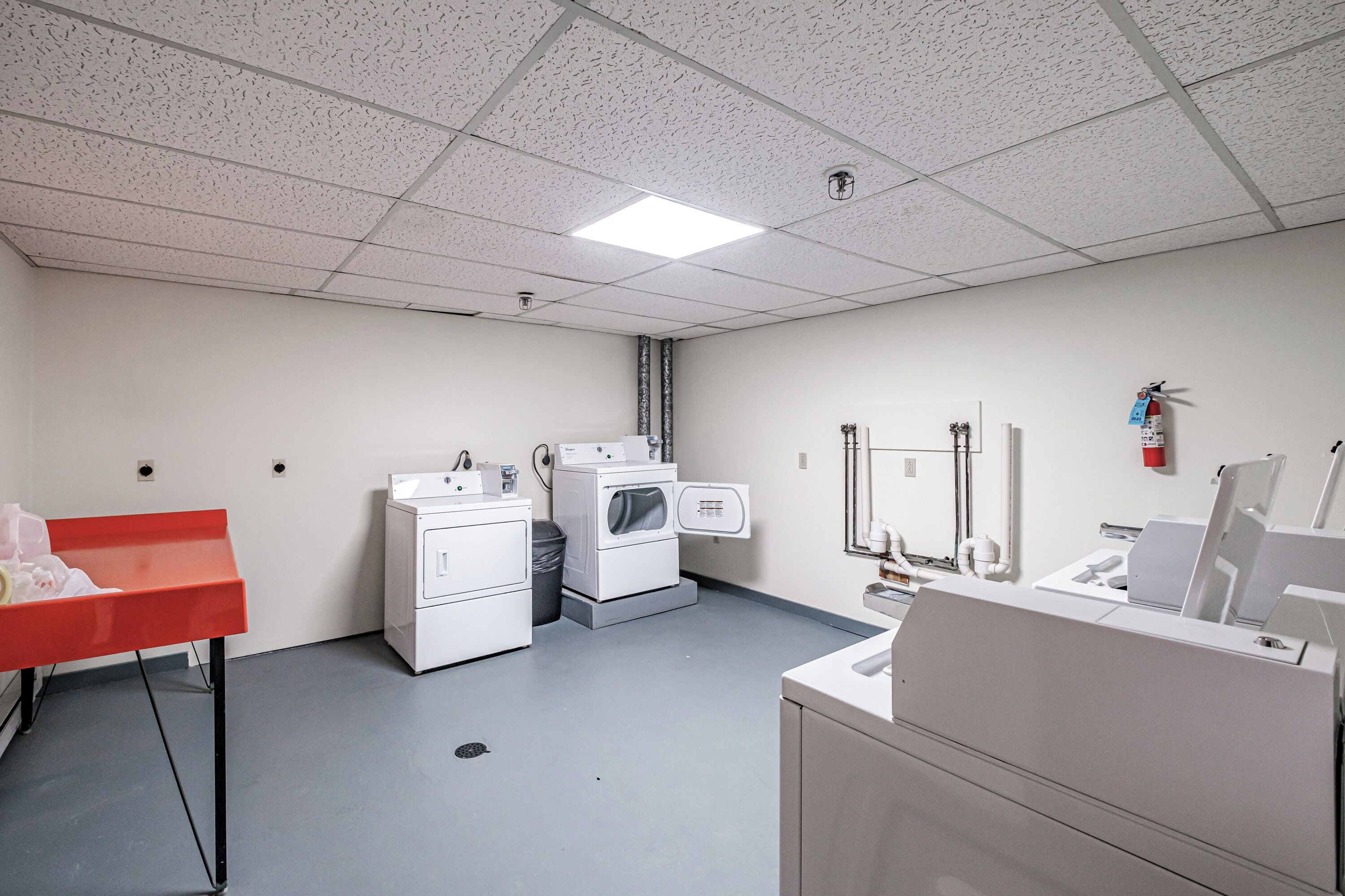 A clean, modern laundry room with a red cart, washing machines, and a sink.