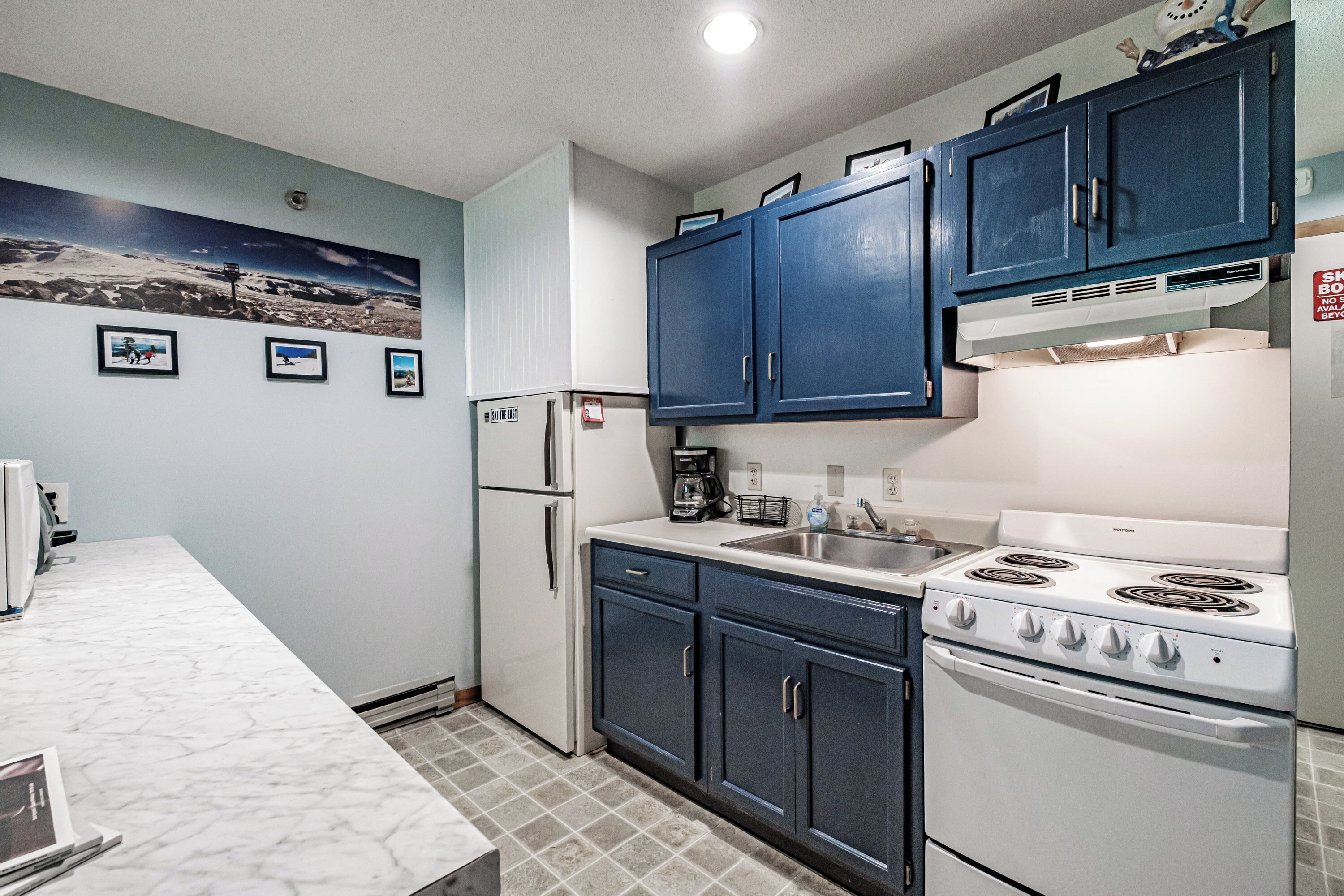 A kitchen with blue cabinets, a white refrigerator, a stove, and a marble countertop.