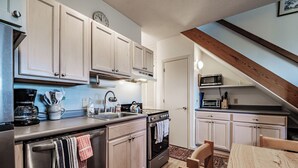 A kitchen with light wooden cabinets, stainless steel appliances, a wooden dining table, and a visible staircase leading to an upper level. - Cascades Ski-in/Ski-out one bedroom sleeps 7 (Newry)