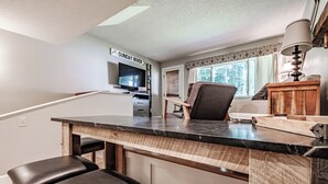 A kitchen with a marble countertop, wooden bar stools, a television, and a sign that reads "SUNDAY RIVER".
