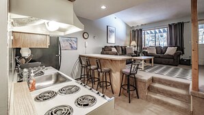 Une cuisine compacte équipée d’une cuisinière, d’un évier et de tabourets de bar. Le salon comprend un canapé et une table à manger.