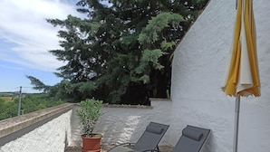 Un balcón con dos sillones de descanso, una planta en maceta y una pared blanca.