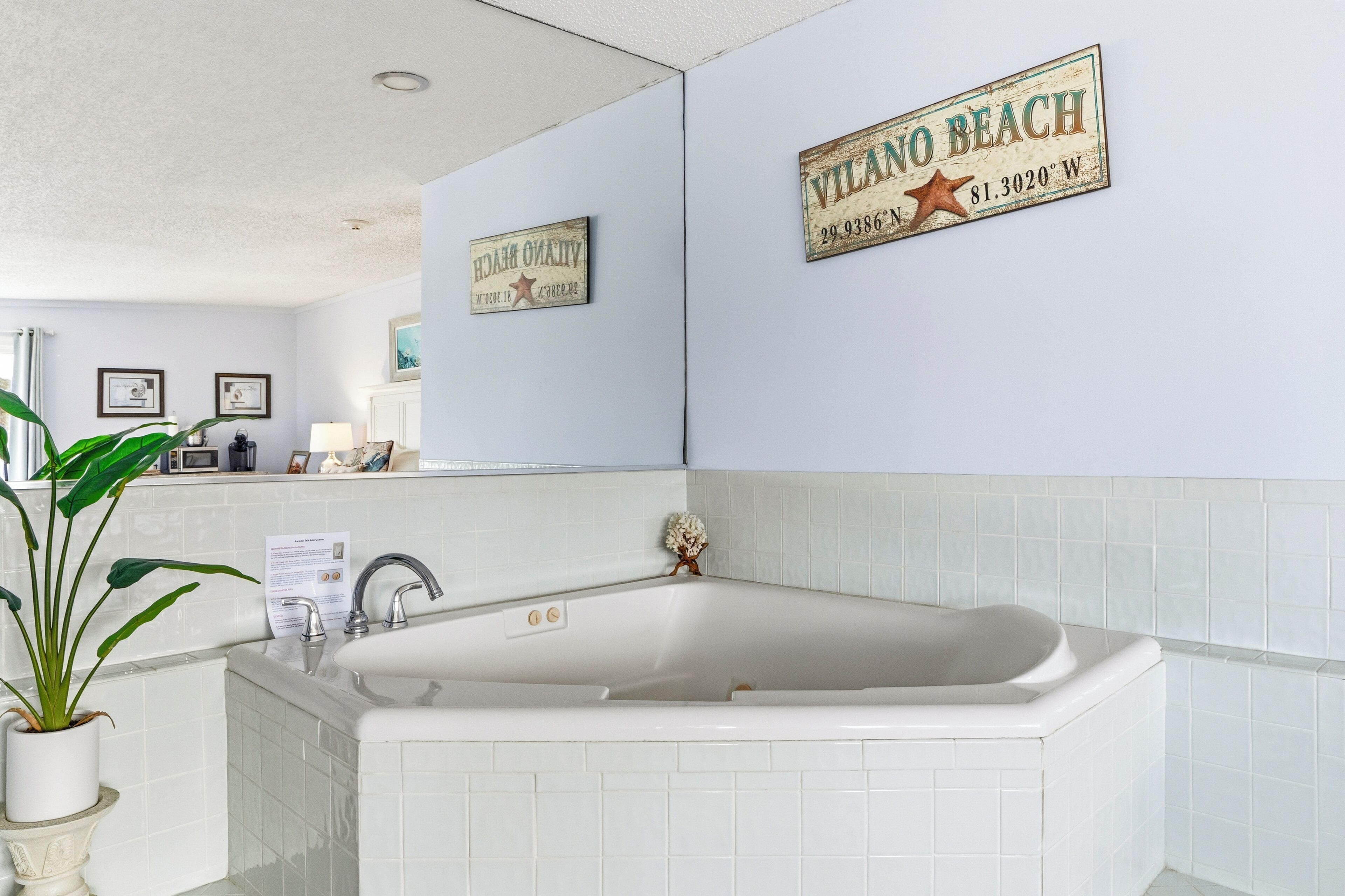 A bathroom with a bathtub, a sink, and a potted plant. There are two framed pictures on the wall and a sign that reads "VILANO BEACH".