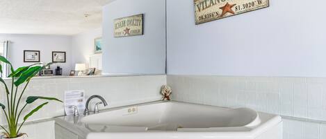 A bathroom with a bathtub, a sink, and a potted plant. There are two framed pictures on the wall and a sign that reads "VILANO BEACH".
