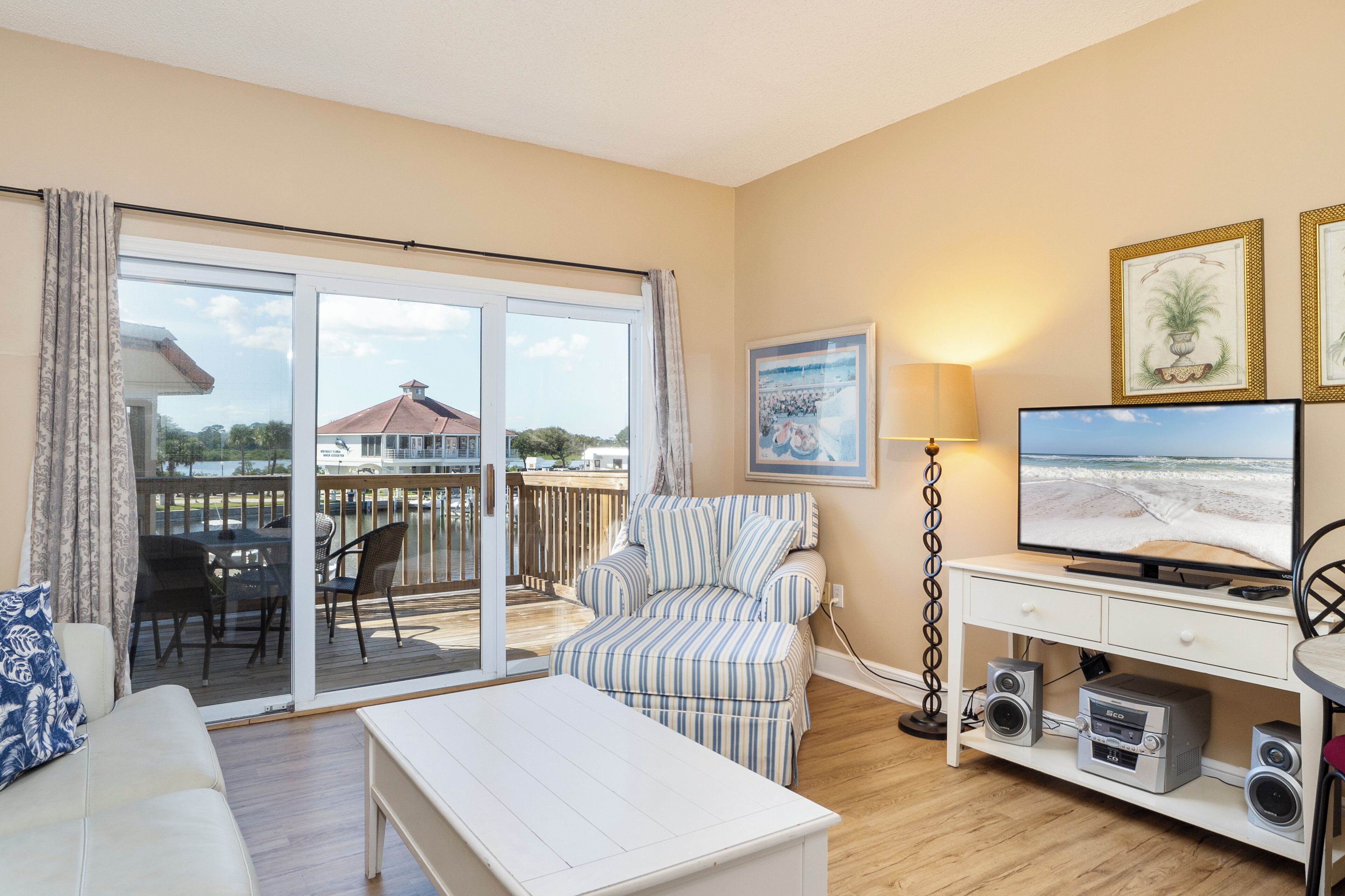 A living room with a sofa, a striped armchair, a TV, speakers, and a sliding glass door leading to an outdoor deck.