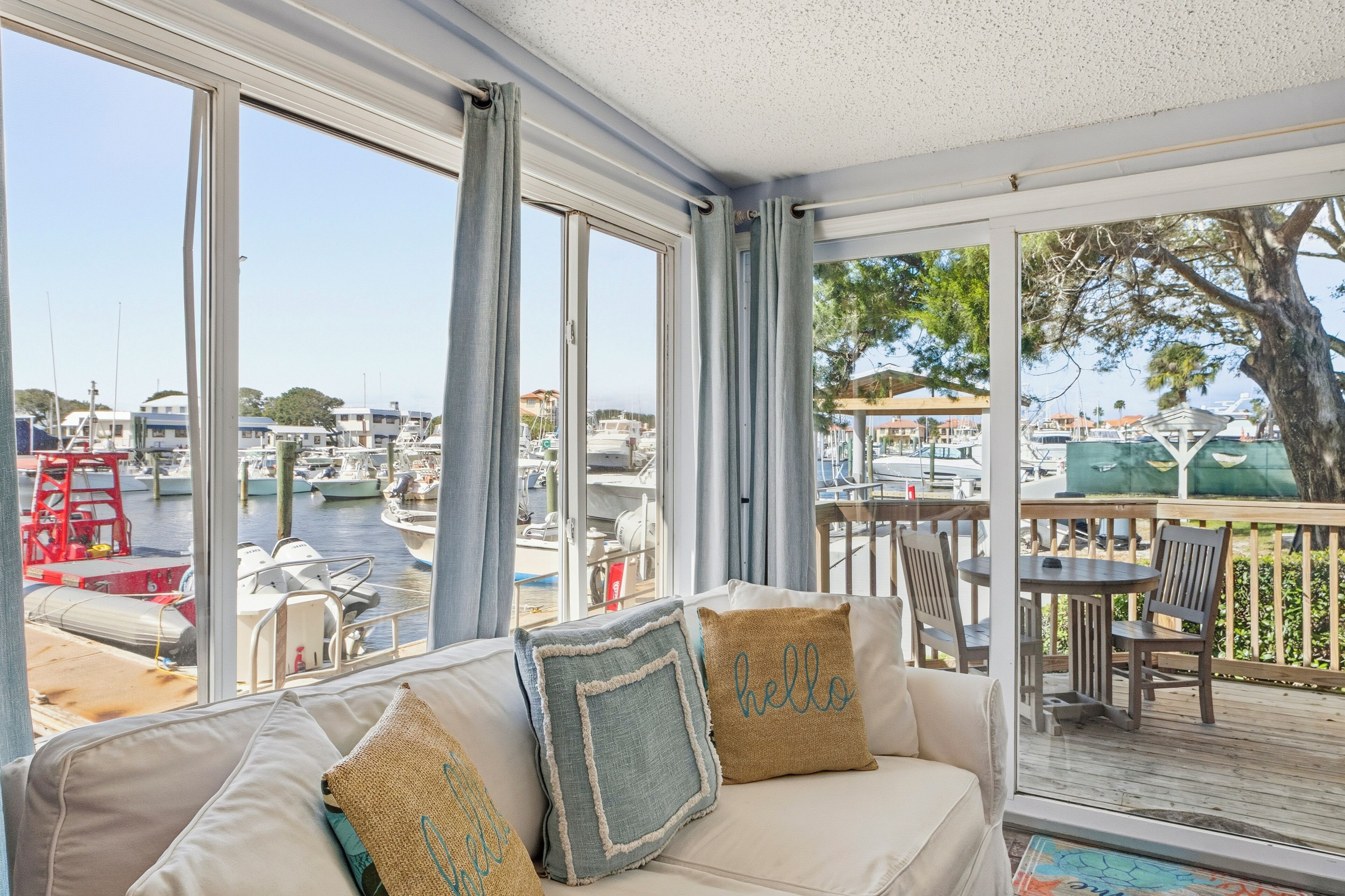 A room with a view of a marina, a sofa with cushions, and a dining area with chairs and a table.
