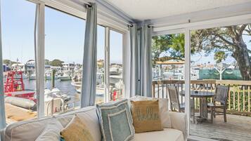 A room with a view of a marina, a sofa with cushions, and a dining area with chairs and a table.