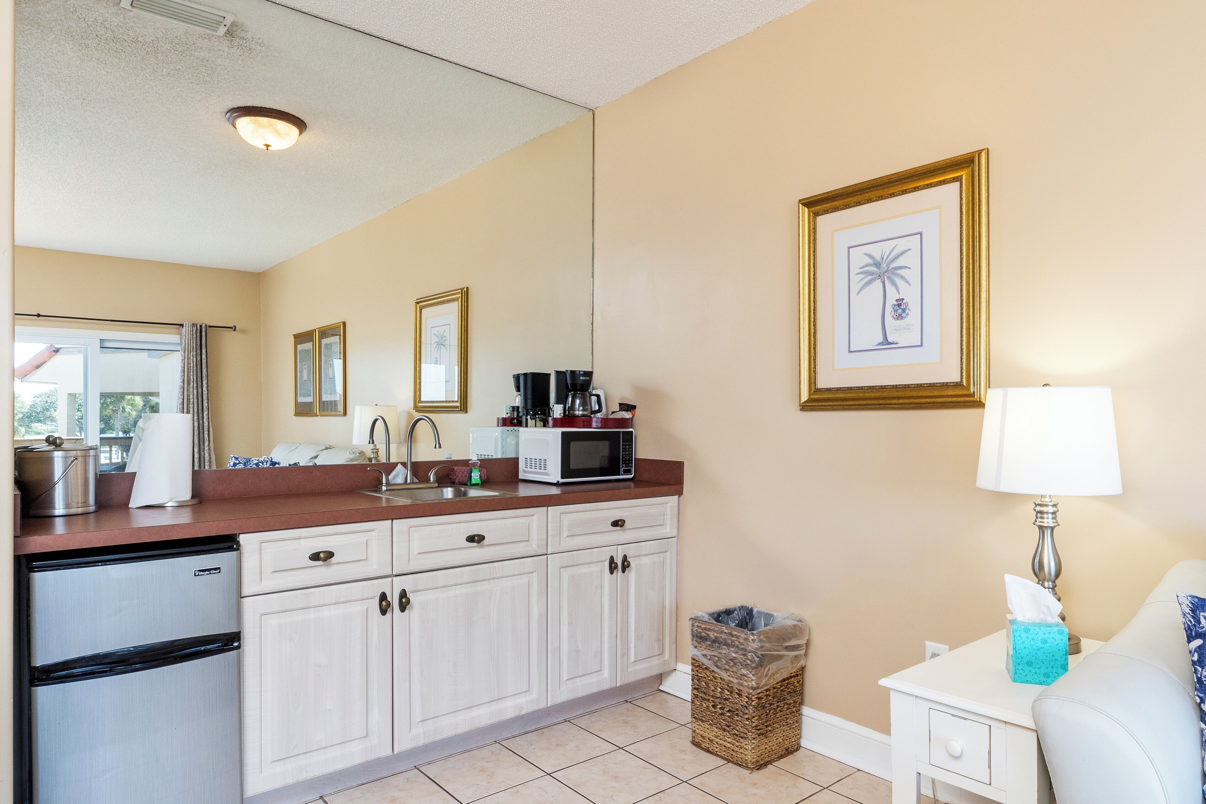 A compact kitchen with white cabinets, a microwave, a coffee maker, and a trash bin.