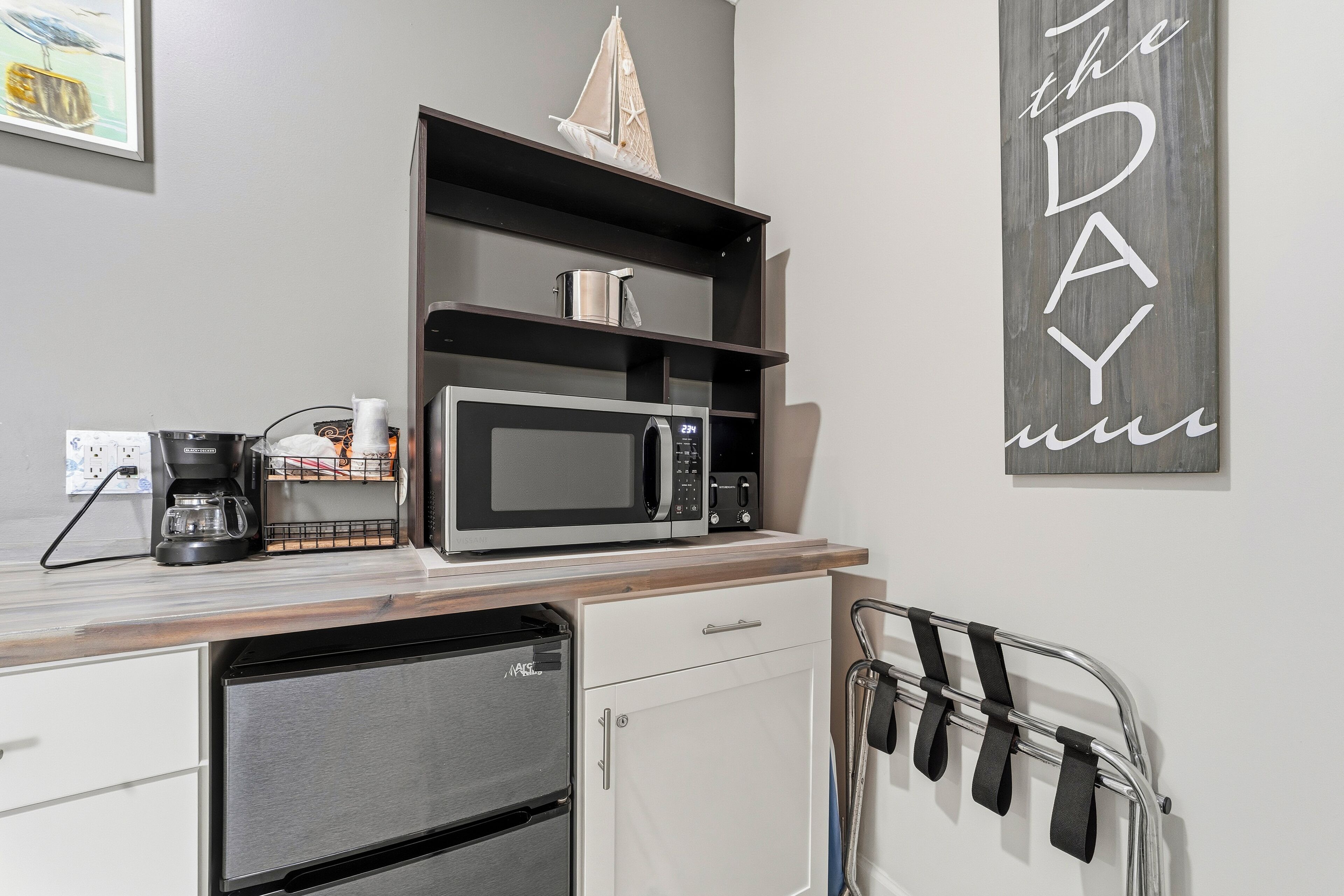 A kitchenette with a microwave, coffee maker, and a small shelf with a ship model.