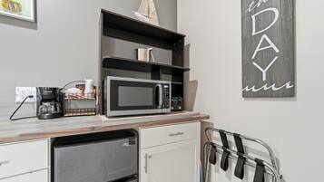 A kitchenette with a microwave, coffee maker, and a small shelf with a ship model.