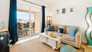 A living room with a sofa, coffee table, and a view of a marina through a glass door. - Inn at Camachee Harbor by Coolvacay (St. Augustine)