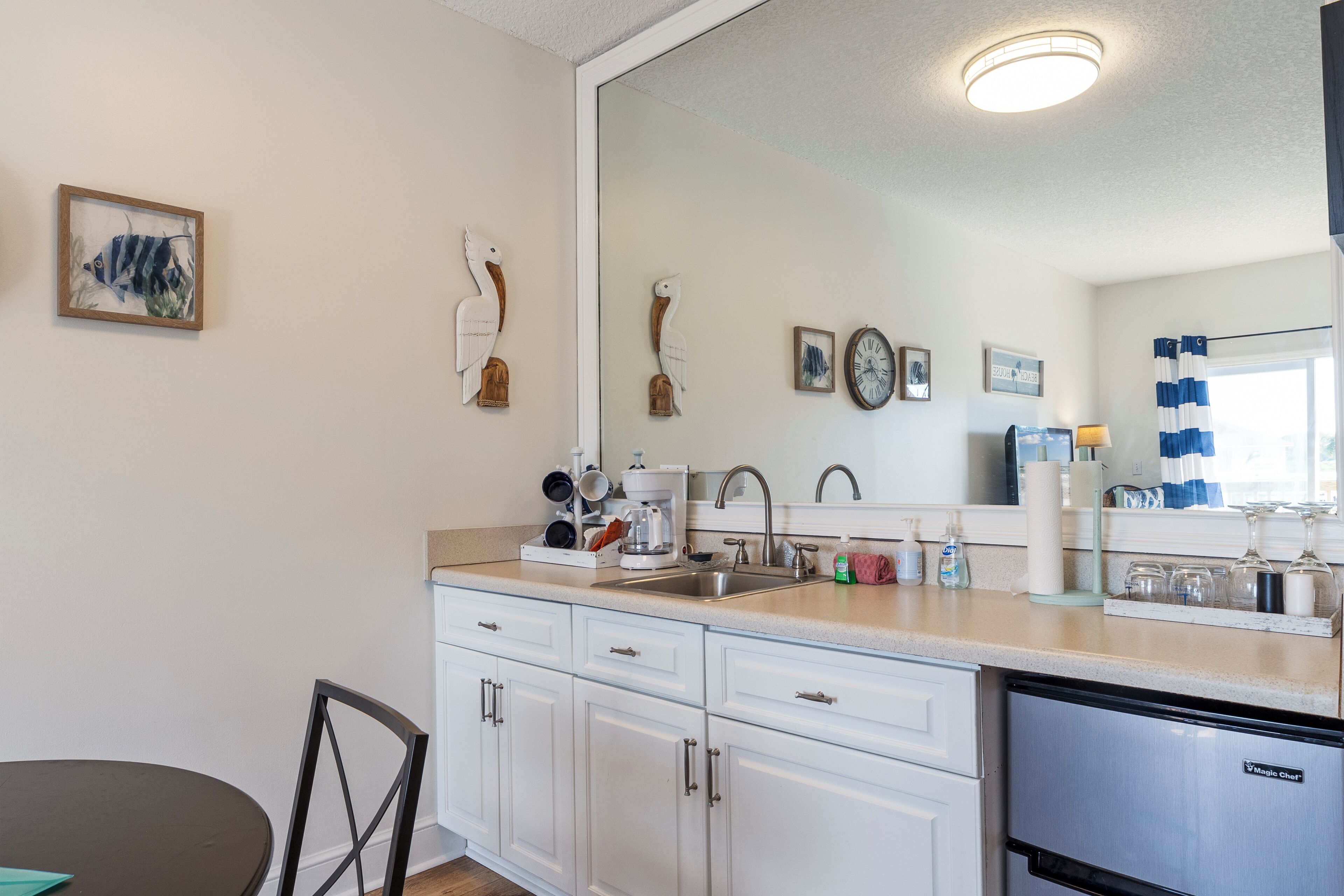 A modern kitchen with white cabinets, a stainless steel refrigerator, and a large mirror above the sink.