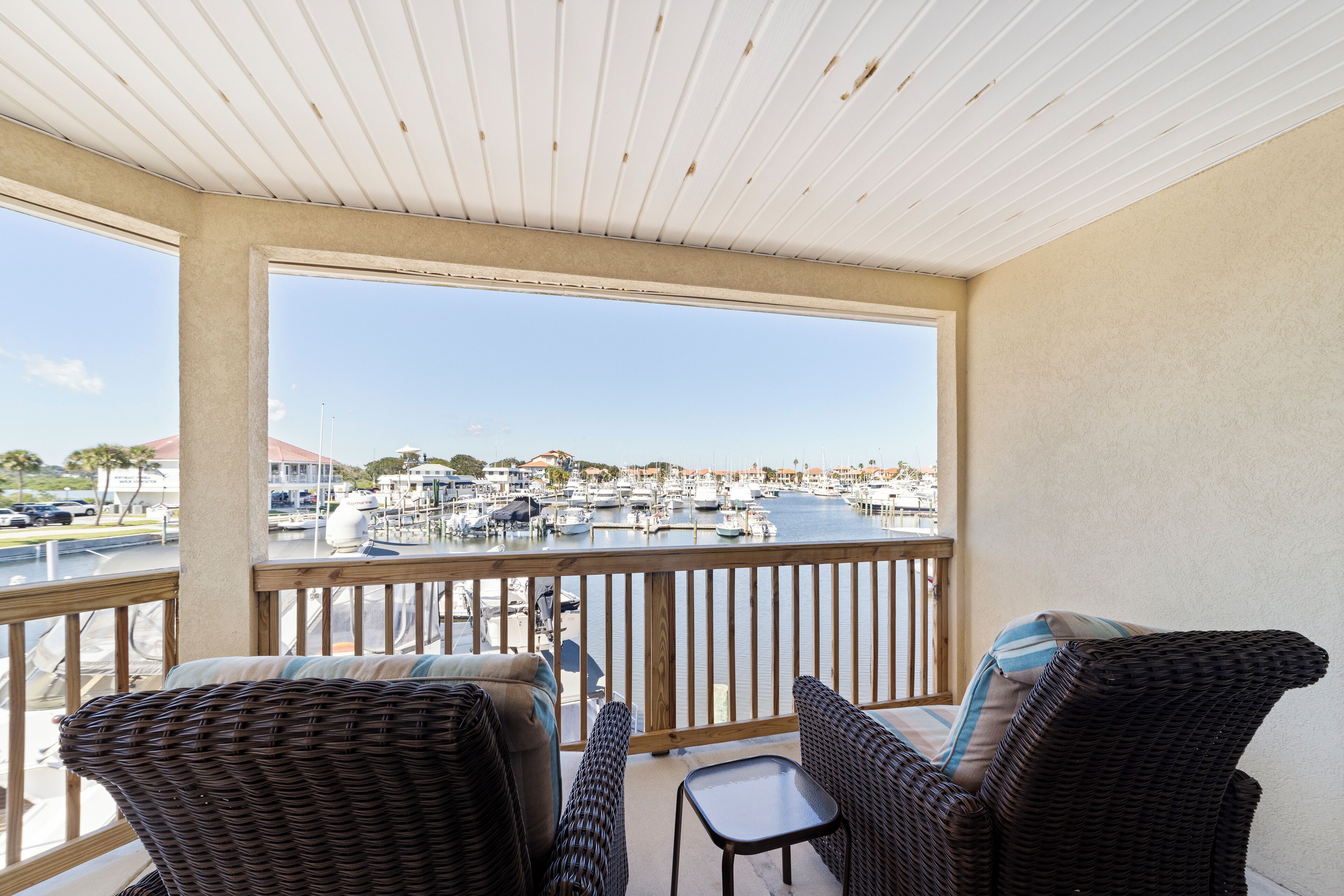 A balcony with wicker furniture, a view of a marina with boats, and a clear sky.