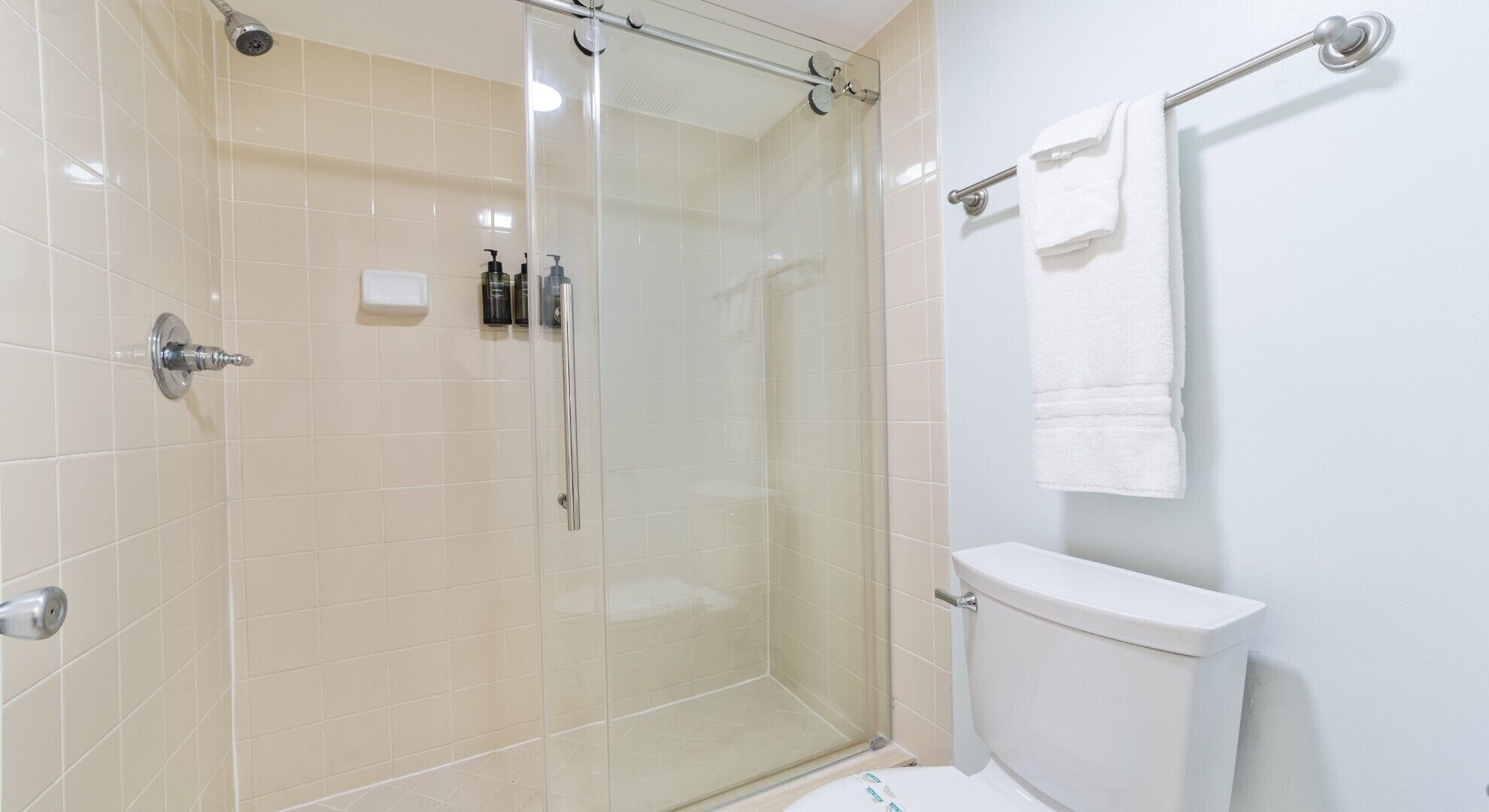Een moderne badkamer met een glazen douchecabine, een toilet en een handdoekhouder.