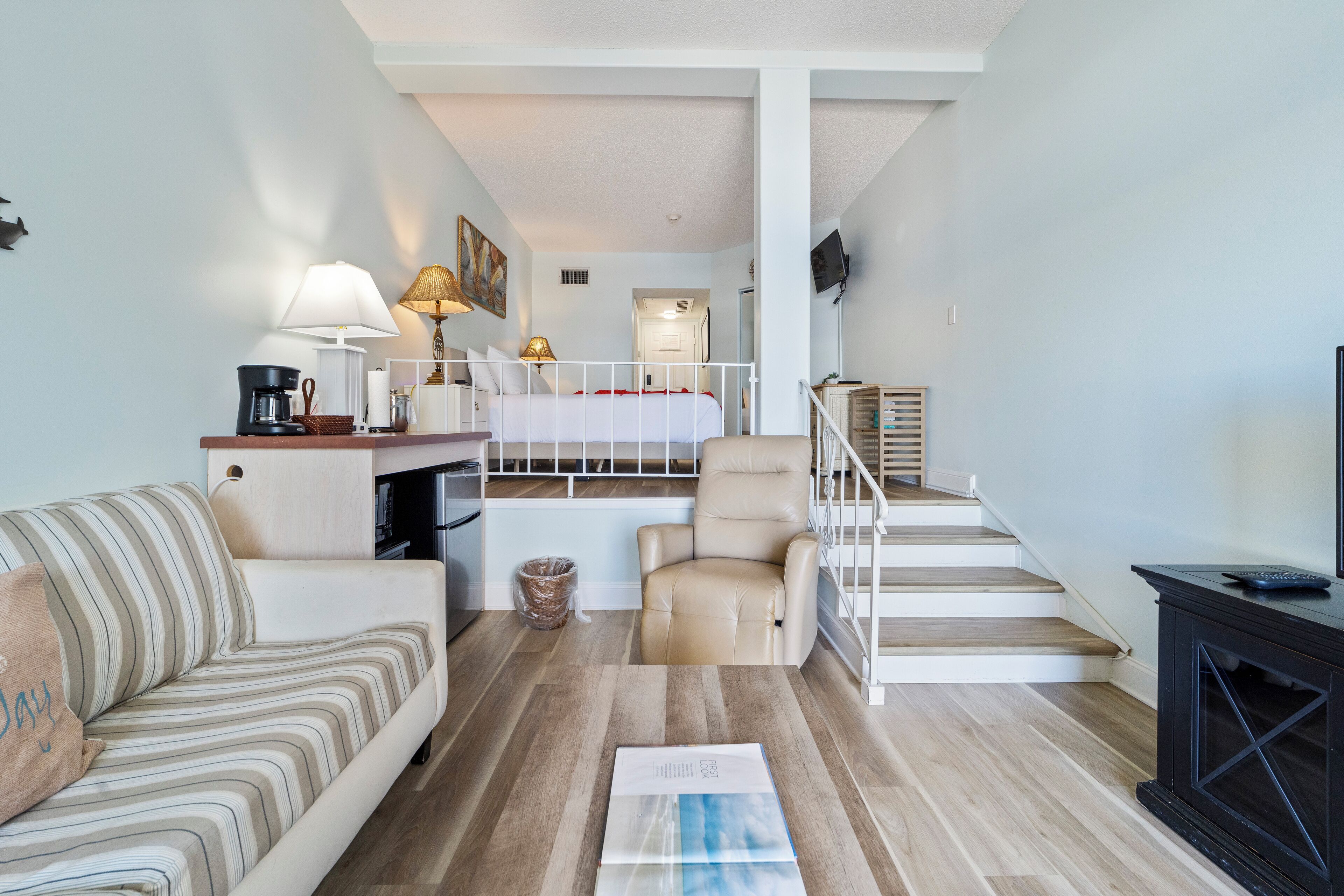 A compact living space with a sofa, a small table, a chair, a staircase, and a television.