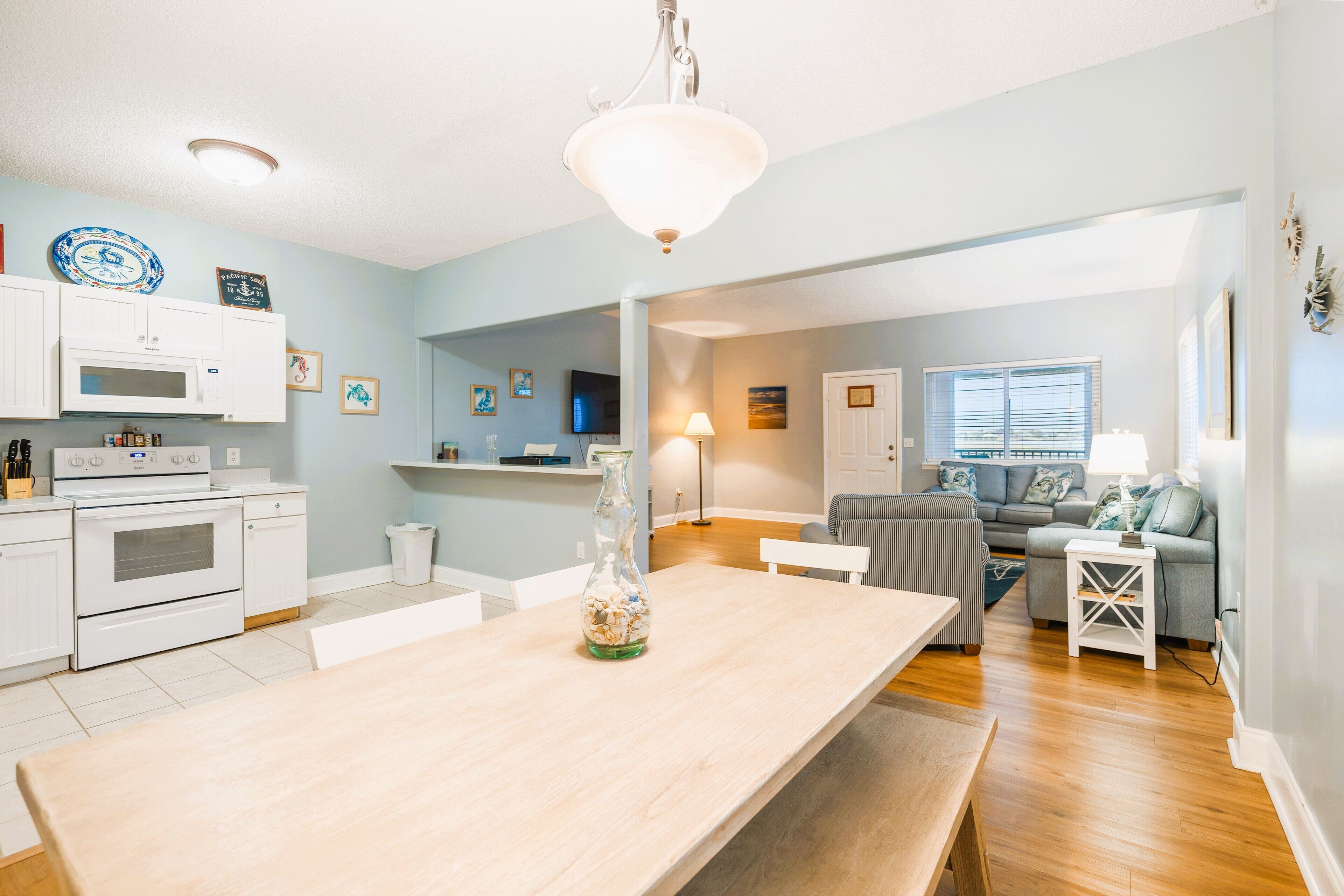 A modern kitchen with white cabinets, a large wooden table, and a hanging light fixture.