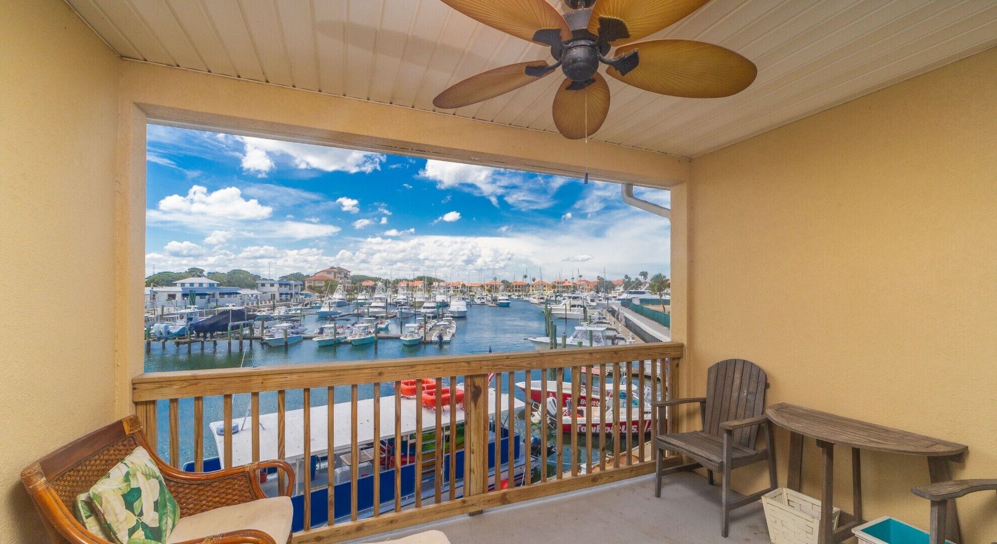 A balcony with a view of a marina, wooden furniture, and a ceiling fan.