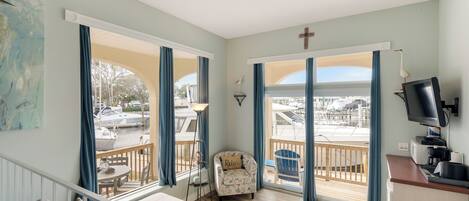 A spacious living area with a balcony, a comfortable sofa, a small table, and a television.