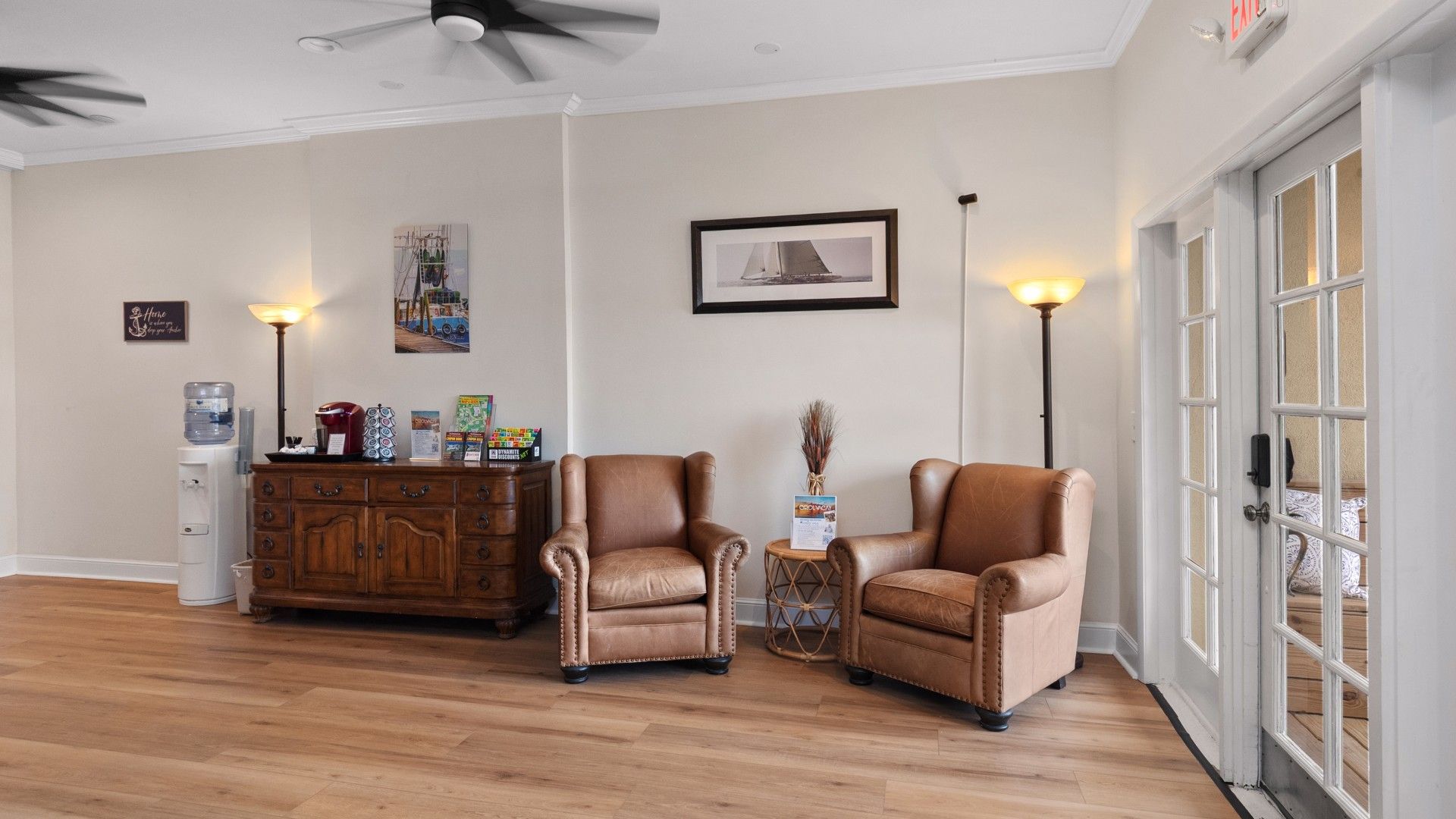 A spacious room with two leather armchairs, a wooden cabinet, and a water dispenser.