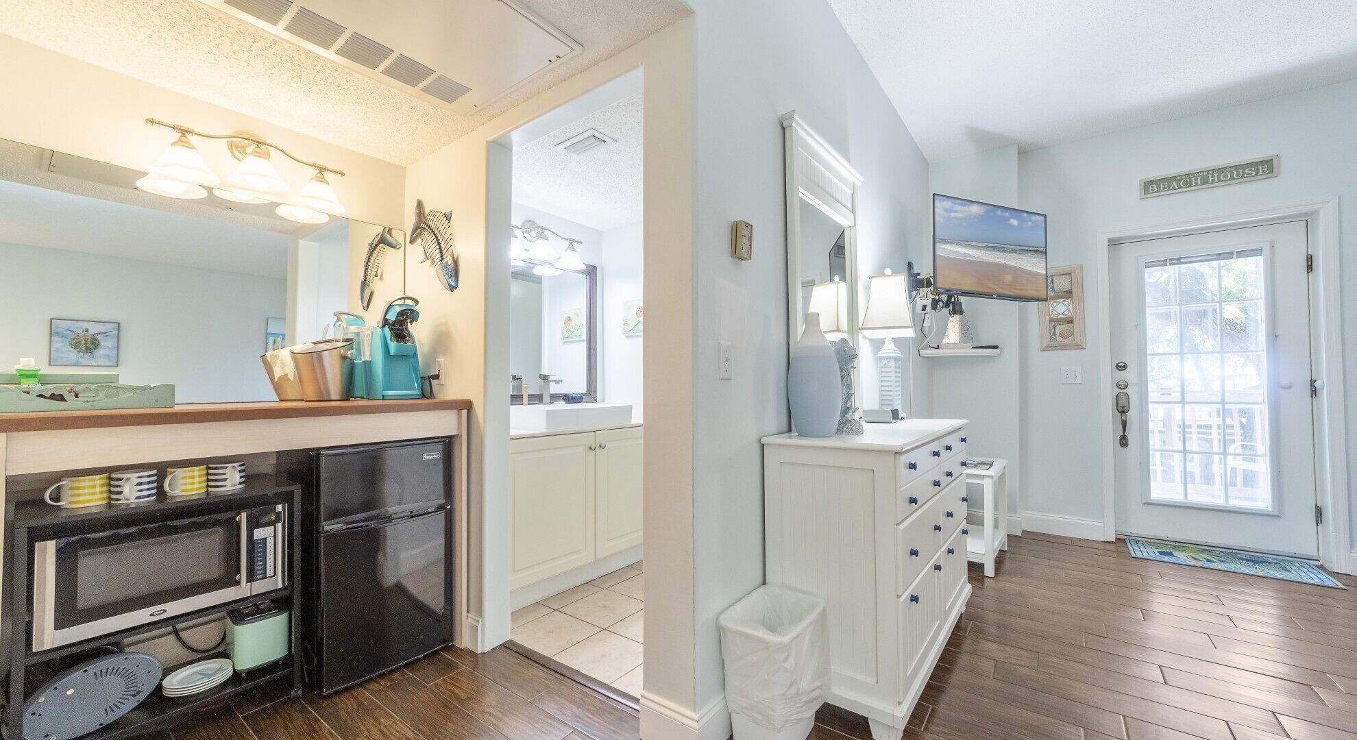 A kitchen with a refrigerator, oven, and microwave. There is a window with a view of the beach.