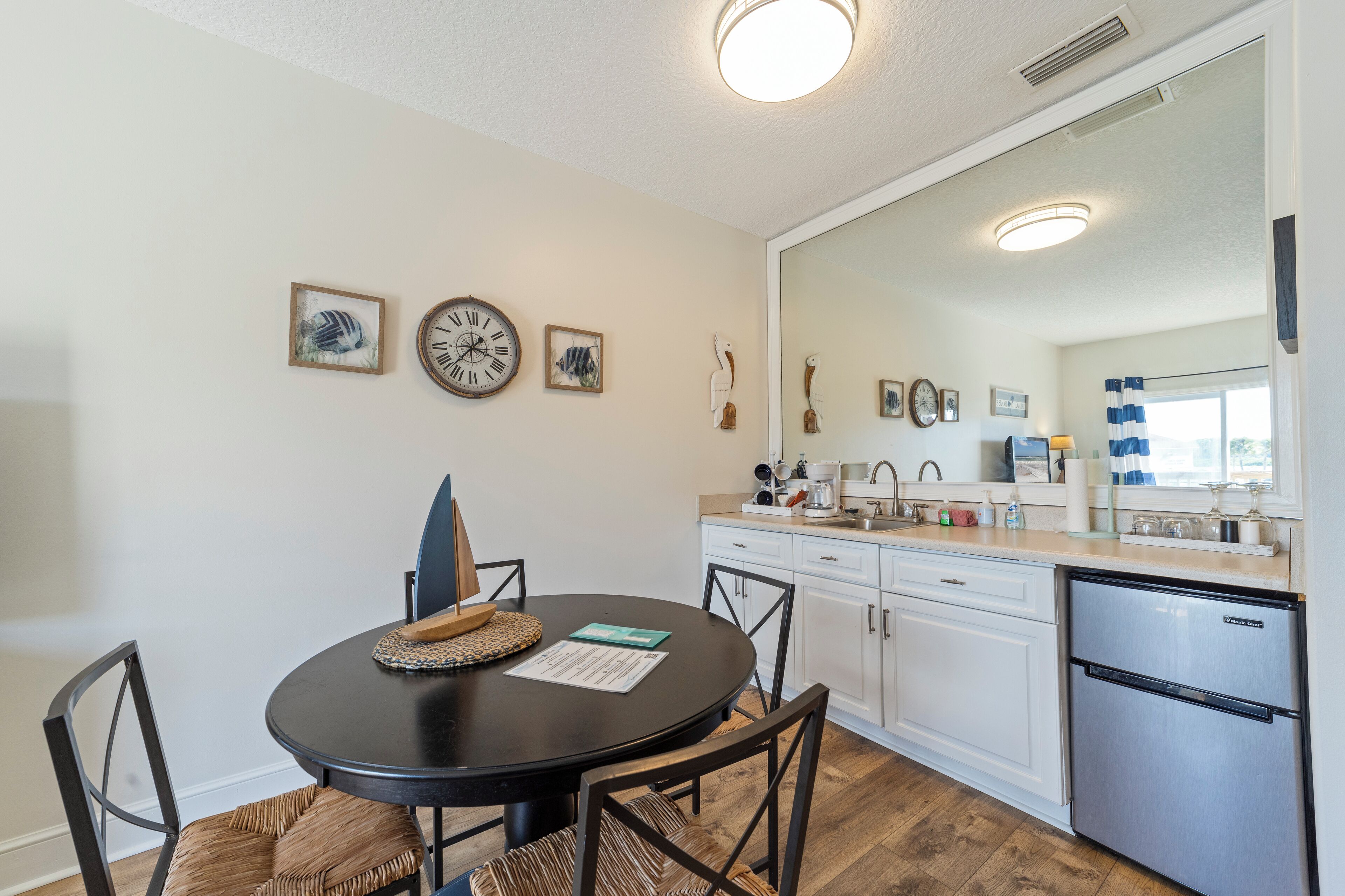 A modern kitchen with white cabinets, a stainless steel refrigerator, and a dining area with a round table and chairs.