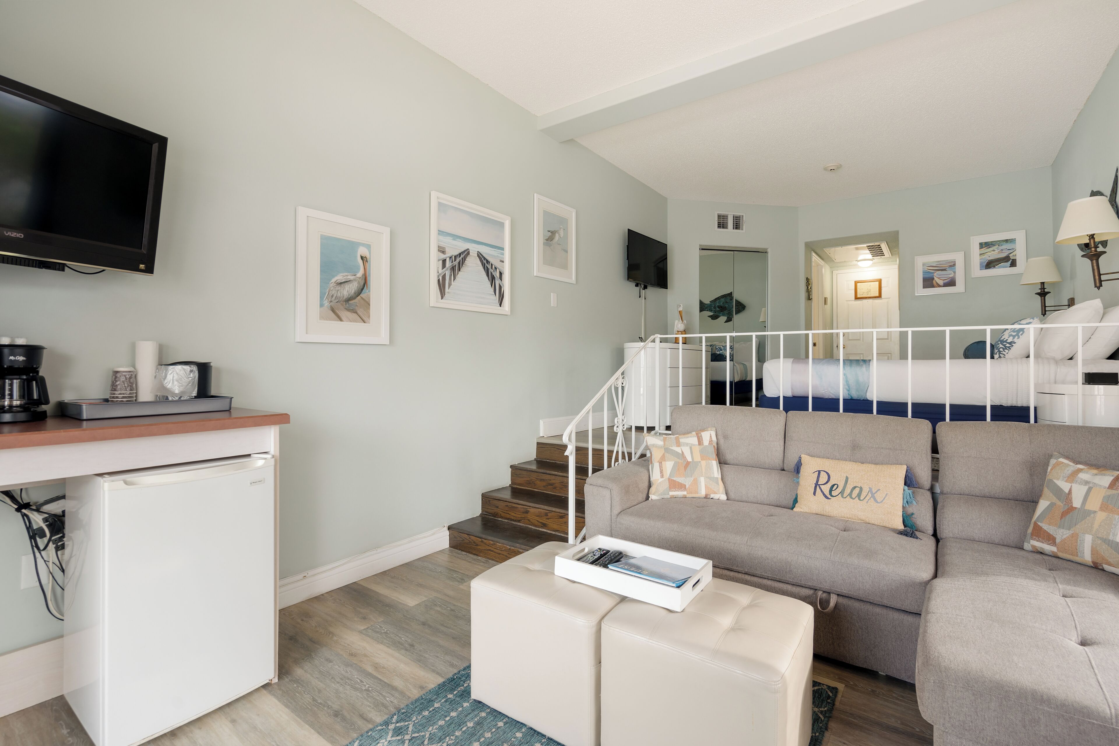 Un salon moderne avec un canapé, une machine à café, un téléviseur et un escalier menant à une autre pièce.
