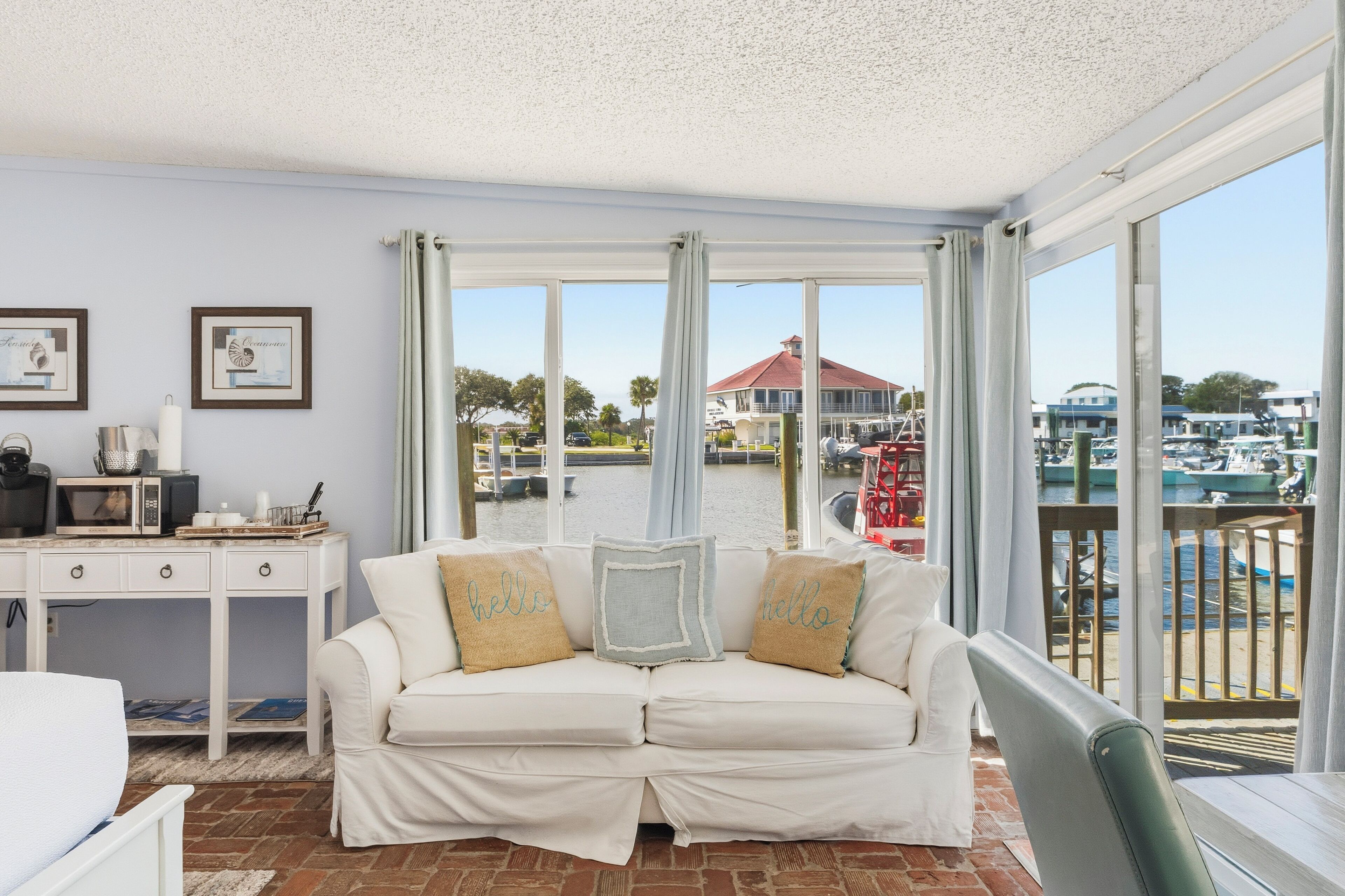 Ein Zimmer mit einem weißen Sofa, einem Schreibtisch mit Mikrowelle und Blick auf eine Marina durch große Fenster.