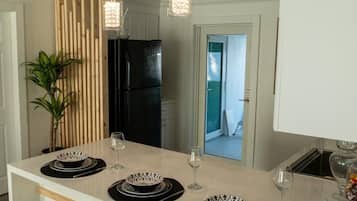 A modern kitchen with a central island, pendant lights, and a view into another room.