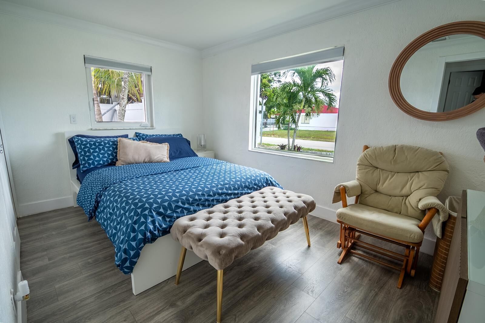 A bedroom with a bed, a chair, a bench, and two windows.