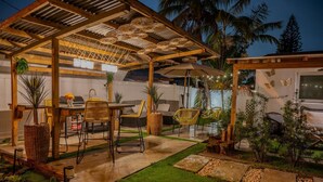 Een terras buiten met een pergola, een zithoek en een eettafel.