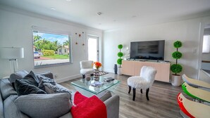 Una sala de estar moderna con un sofá, una mesa de centro de vidrio, un televisor y plantas decorativas.