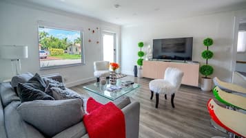 A modern living room with a sofa, a glass coffee table, a TV, and decorative plants.