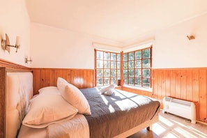A bedroom with a bed, pillows, a window with a view of trees, and a heater.