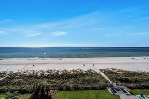 A beach with a clear sky, sandy shore, and a grassy area with a fence.