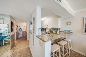 A kitchen with a granite countertop, white cabinets, and a clock on the wall. - FREE Golf & Perks! Mariner West 609 Beachfront Swimming Pool, Tennis, Grills! (Panama City Beach)