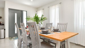 Un coin repas avec une table en bois et des chaises grises, une plante en pot et, au fond, une porte grise.