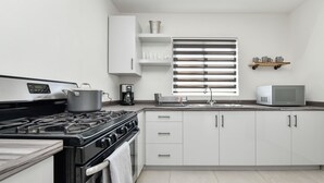Une cuisine moderne avec des meubles blancs, une cuisinière, un four à micro-ondes et une fenêtre équipée de stores.