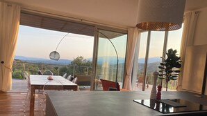 Un espace repas moderne avec une grande table et des chaises, un îlot de cuisine et une vue sur les montagnes grâce à de grandes fenêtres.