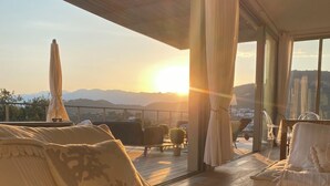 Un espace de détente extérieur accueillant, avec un canapé et des fauteuils, une table et une vue sur le coucher de soleil sur les montagnes.