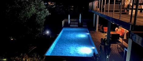 Ein Schwimmbecken mit Holzterrasse und Sitzgelegenheiten im Freien.