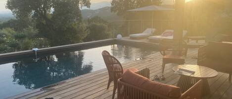 A wooden deck with a pool, lounge chairs, and a table.