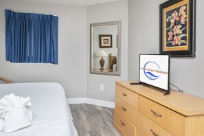 A hotel room with a bed, a wooden dresser, a mirror, a framed picture, and a sign on the wall.