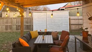 An outdoor patio with a wooden ceiling, string lights, a sofa, chairs, and a table.