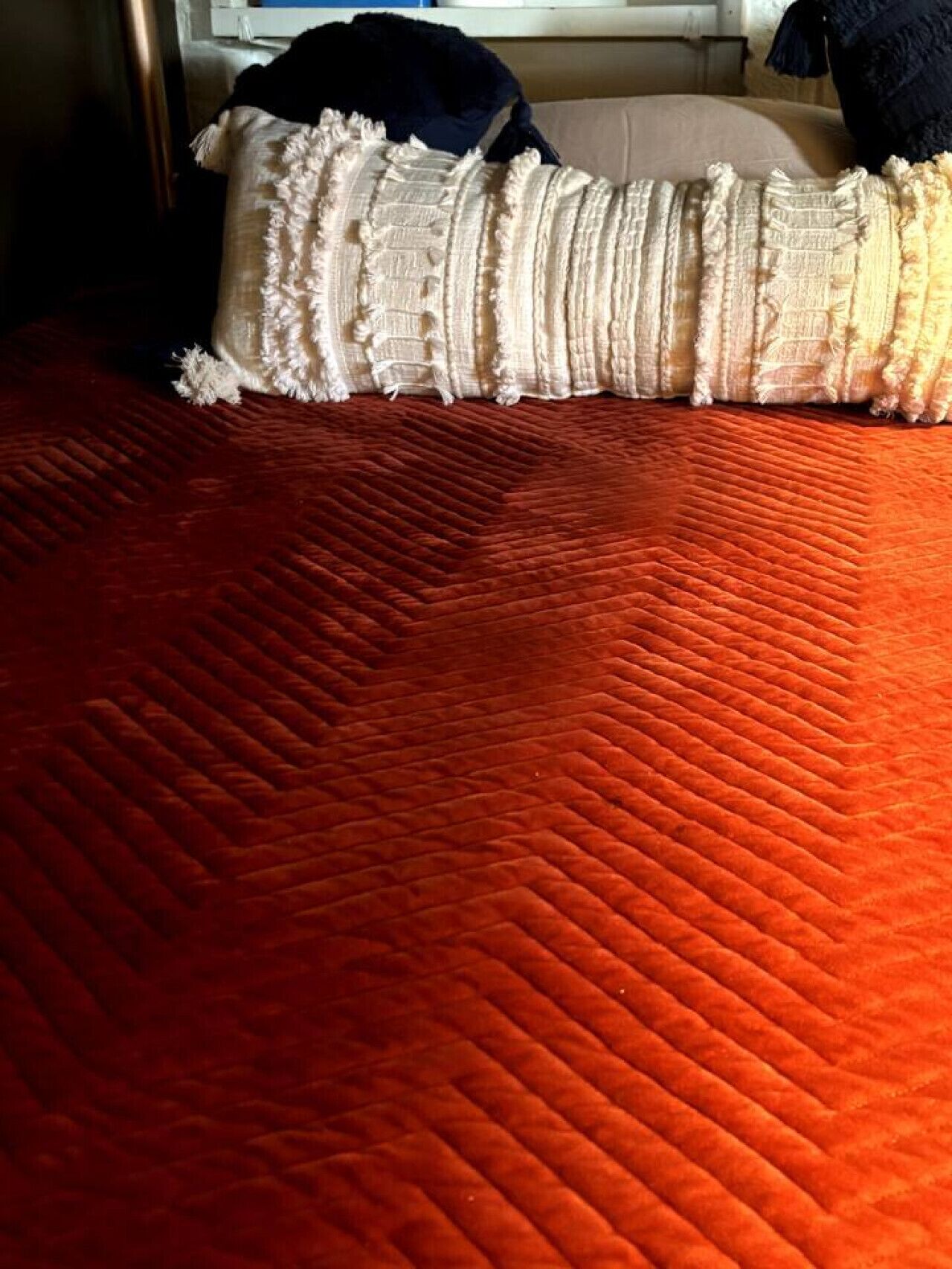 A bed with a red quilt and a white, fringed pillow.