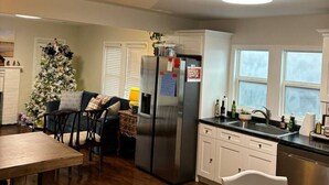 A modern kitchen with a central island, white cabinetry, a stainless steel refrigerator, and a dining area with a Christmas tree.